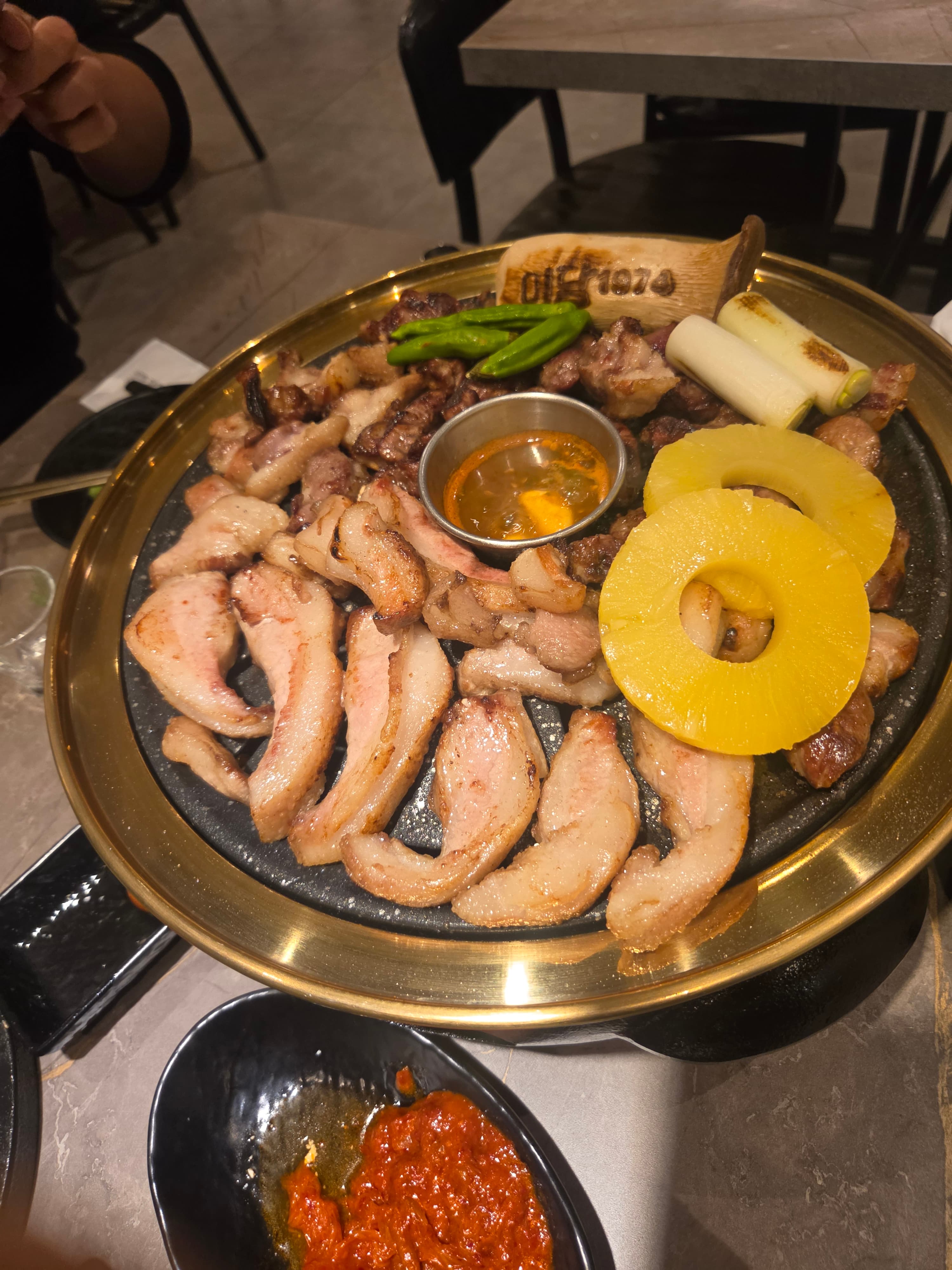 Grilled pork belly, neck, and pork jowl on a brass charcoal grill at Midam 1974, with pineapple, shishito peppers and a branded wooden Midam 1974 marker